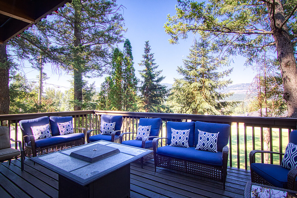 Outside patio deck with a fire table and 8 patio chairs with blue pillowing.