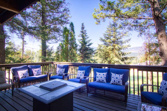Outside patio deck with a fire table and 8 patio chairs with blue pillowing.