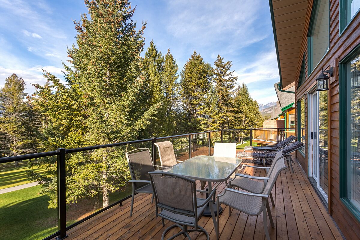 Patio with outdoor furniture, table and chairs overlooking green trees and grass.