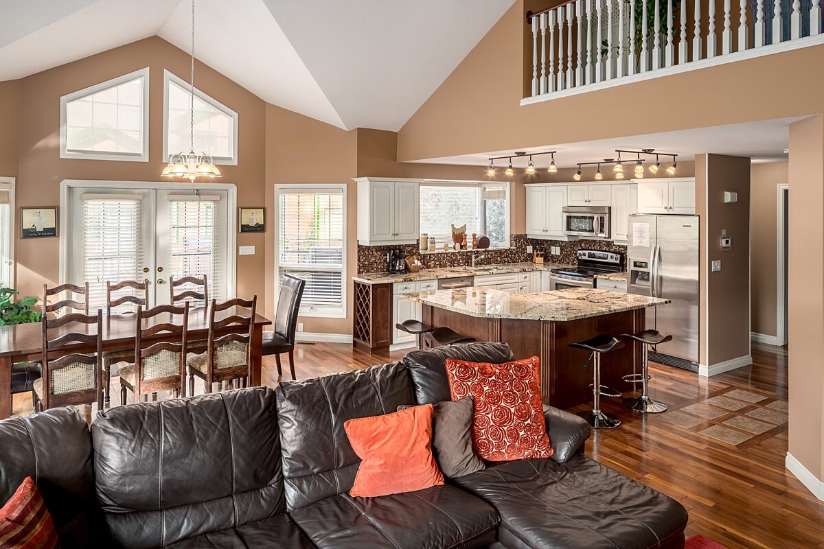 Living room with black leather couch. Dining room area and kitchen to the rear.