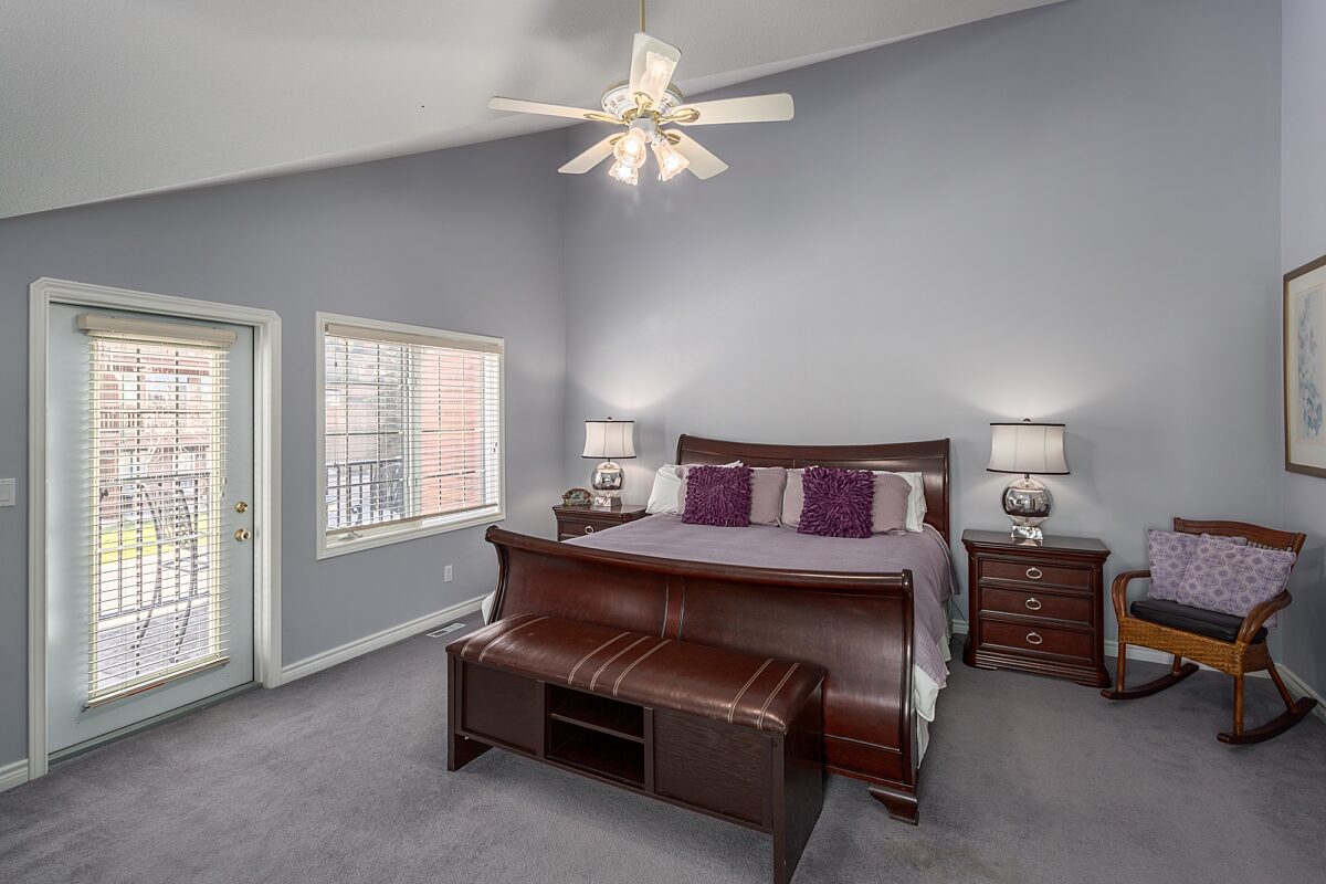 Master bedroom with king bed. Grey walls and high ceiling, two bedside tables with lamps.