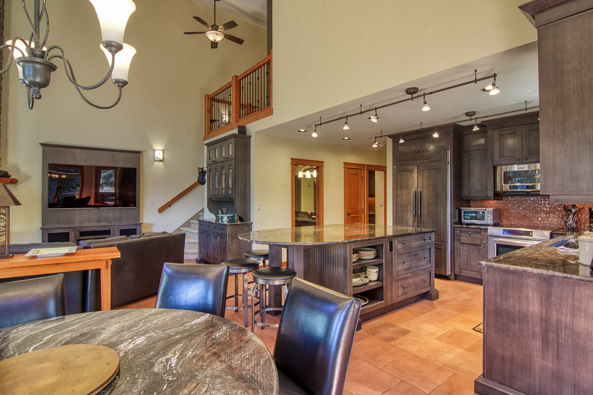 Kitchen and living room area. Dining table in the foreground and large kitchen with an island, fridge, and stainless steel appliances .