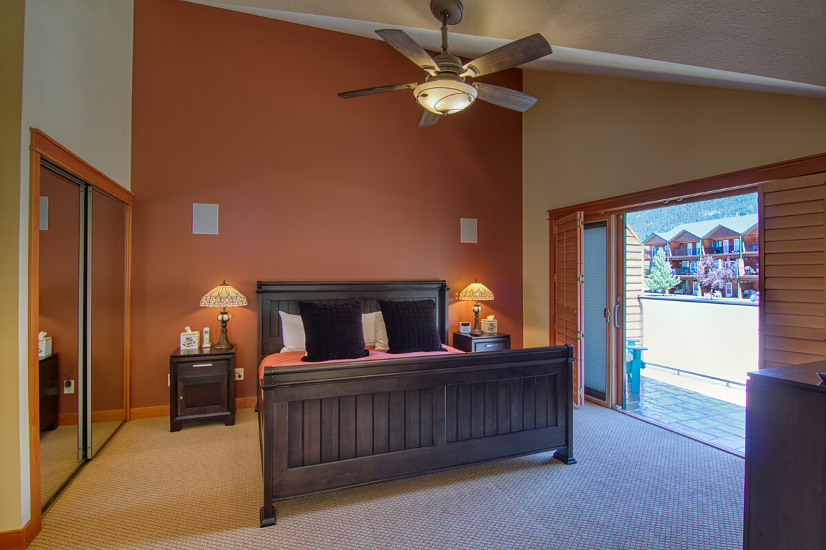 Bedroom with dark wooden frame king bed and salmon walls. Large window with a mirrored closet opposite.
