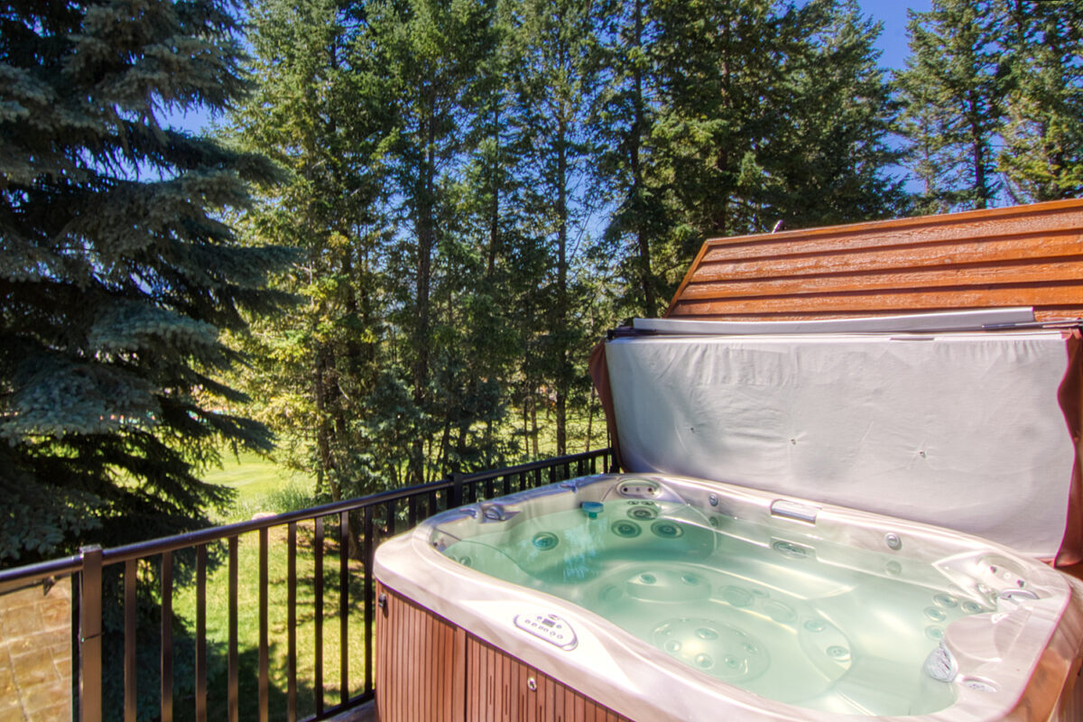 Wood paneled porch hot tub on a deck with its lid off. The water in the hot tub is clear. Porch overlooks treed area.