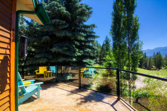 Large deck porch area with blue and yellow patio furniture. Overlooking a gold course, blue sky and mountains.