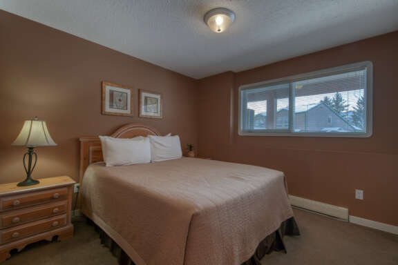 Bedroom with queen bed, bedside table with lamp, and window to the right.