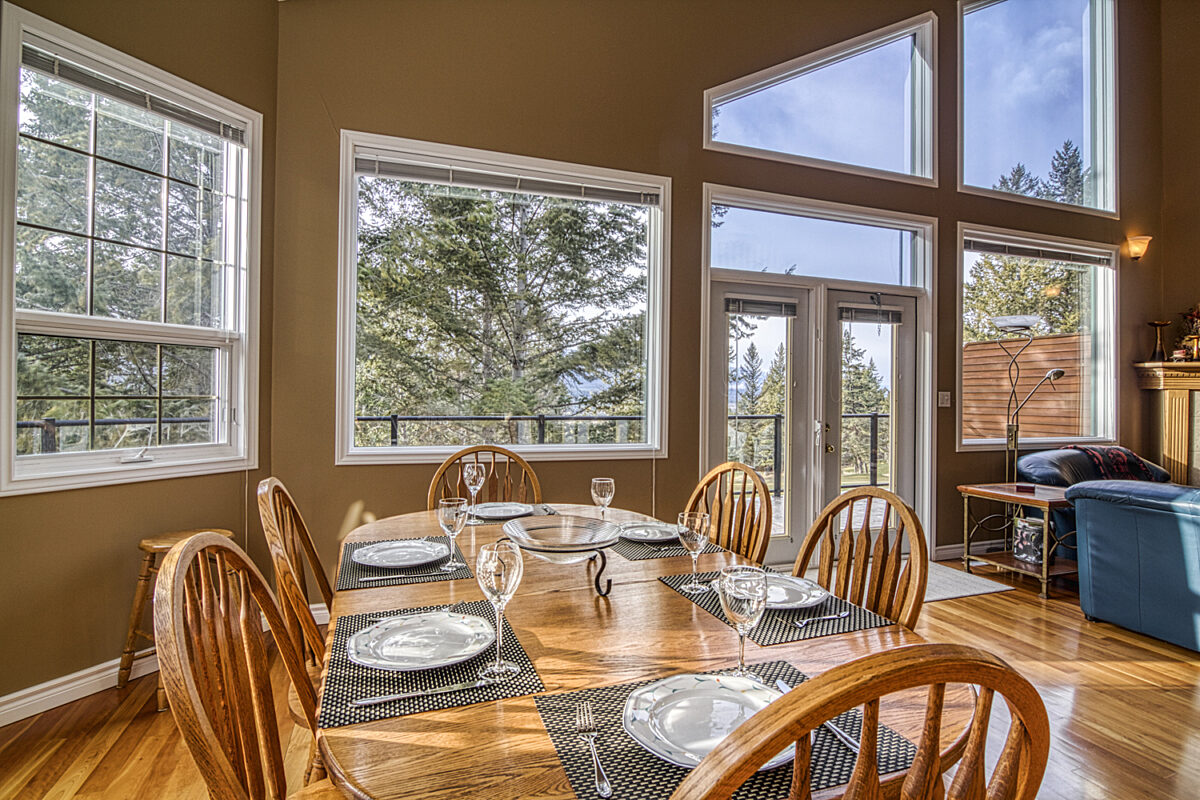 Dining room table set with plates, glasses, and cutlery. Windows and tall ceilings around the dining area.