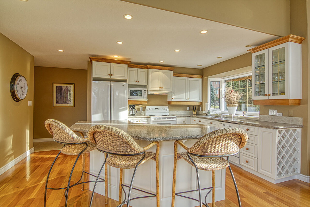 Spacious kitchen and kitchen island with light wood and white detailing. Three barstools.