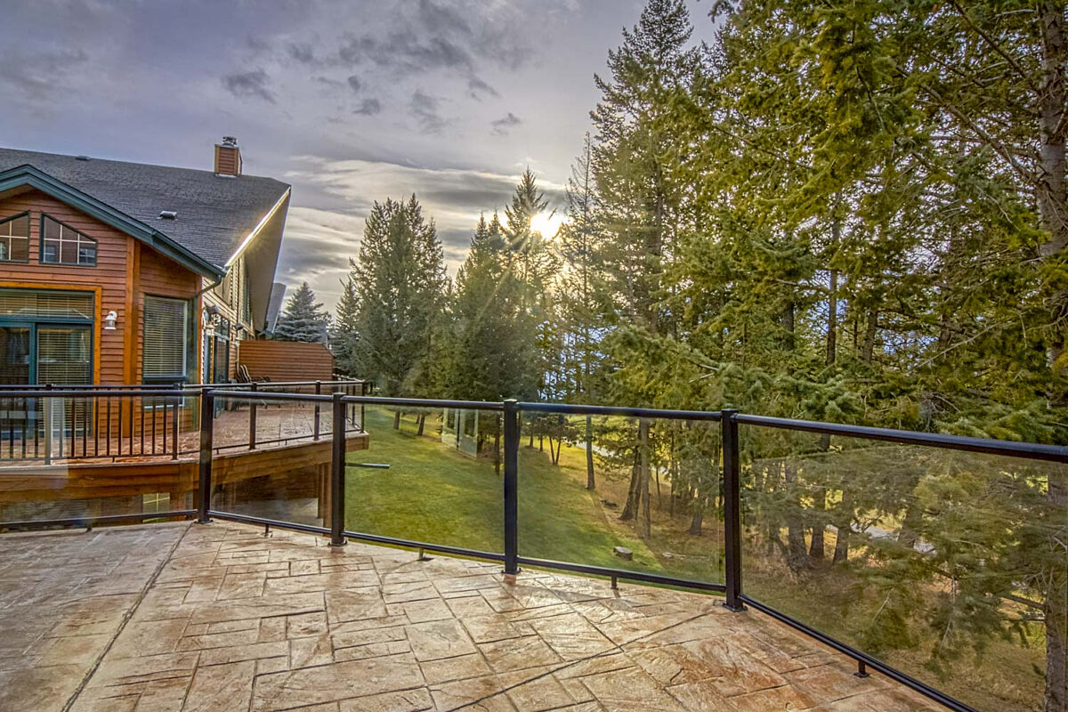 Wraparound deck with glass panelling on the guardrails. Views of the neighbouring house and trees, golf course in distance.