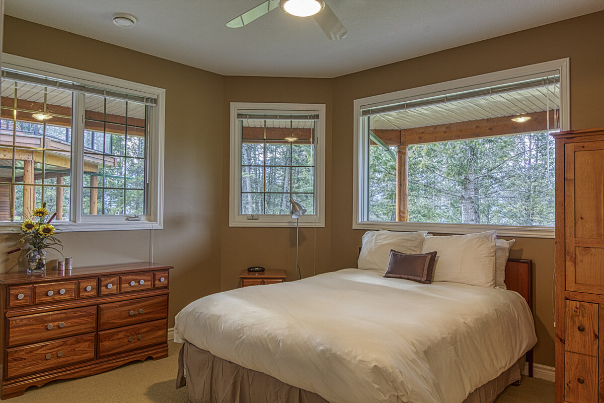 Bedroom with queen bed with white bedding and three windows in the bedroom.