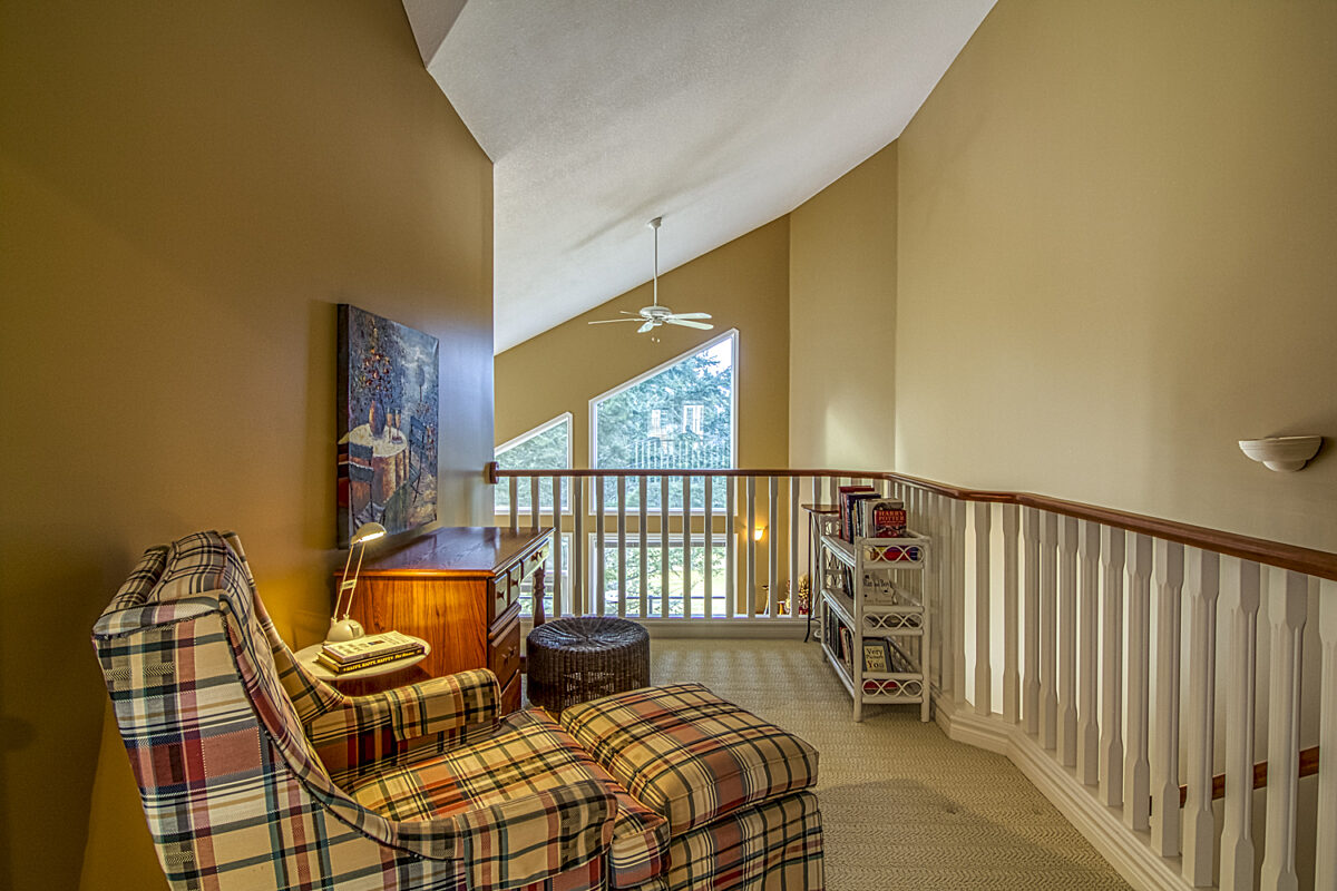 Loft area of a home with a reading chair, bookshelf, and railing overlooking the rest of the house.
