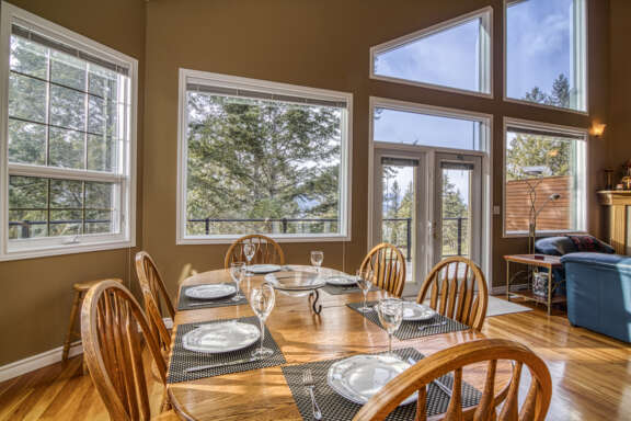 Dining room table set with plates, glasses, and cutlery. Windows and tall ceilings around the dining area.