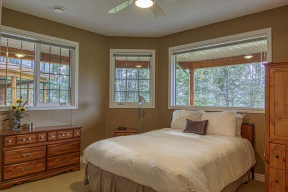 Bedroom with queen bed with white bedding and three windows in the bedroom.