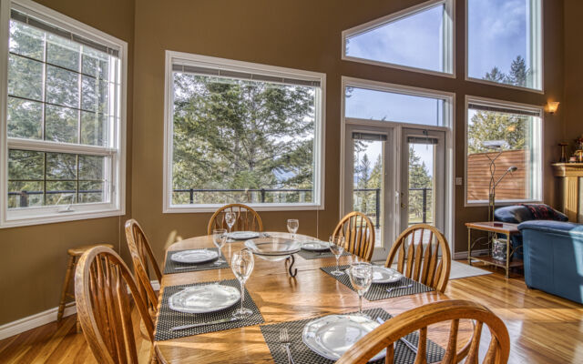Dining room and living room as viewed from the loft above. Light wood dining table and chairs, blue couch and chair, rug, coffee table, and fireplace.