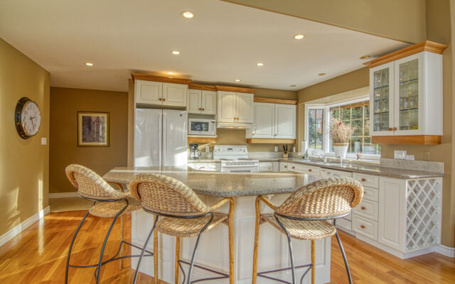 Dining room and living room as viewed from the loft above. Light wood dining table and chairs, blue couch and chair, rug, coffee table, and fireplace.