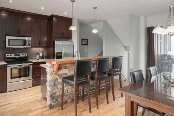 Kitchen with island, barstools, appliances, and dining table to the foreground.