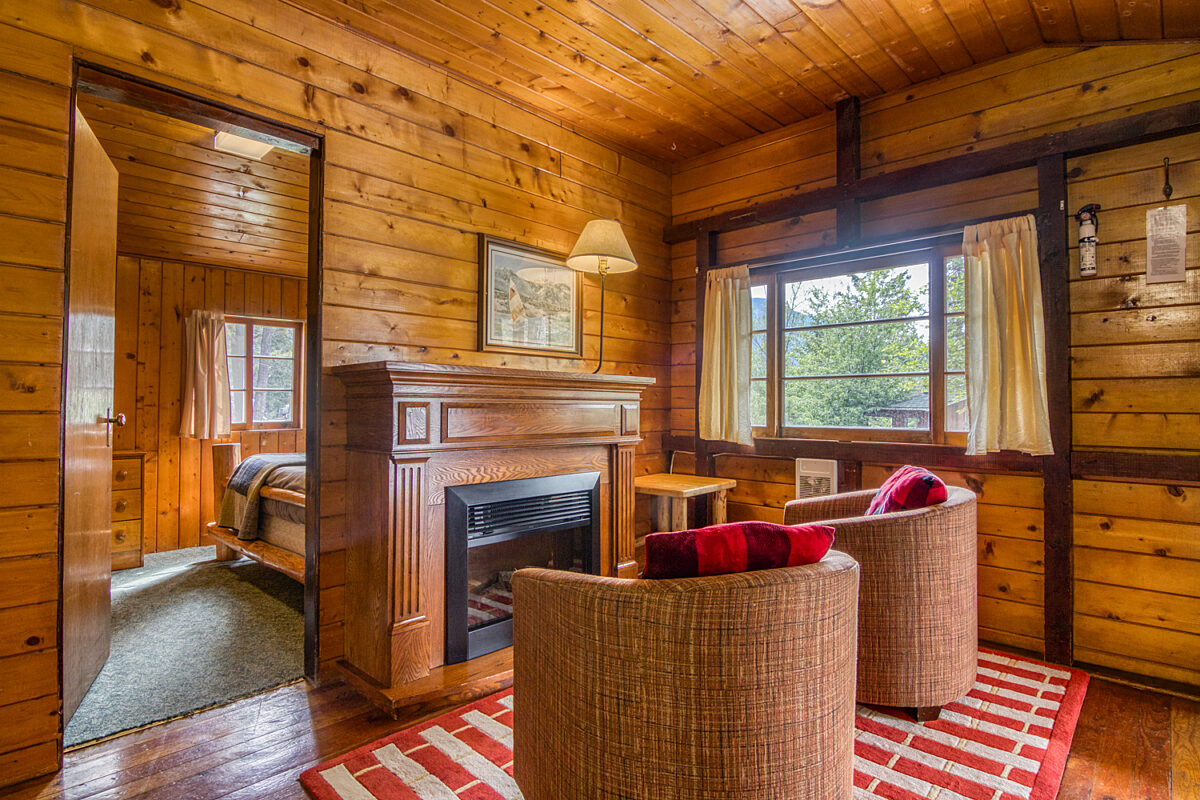 Living room with fireplace. Wooded panelling and two chairs, dining room in background.