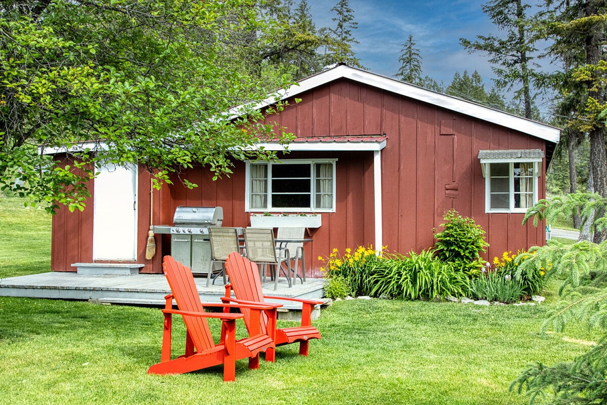 Small red cabin with two red outdoor lounge chairs outside. Trees and greenery surrounding.