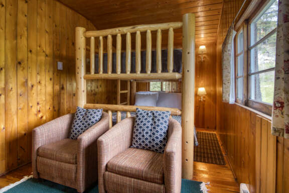 Double bunk bed bedroom with two chairs and window to the right.