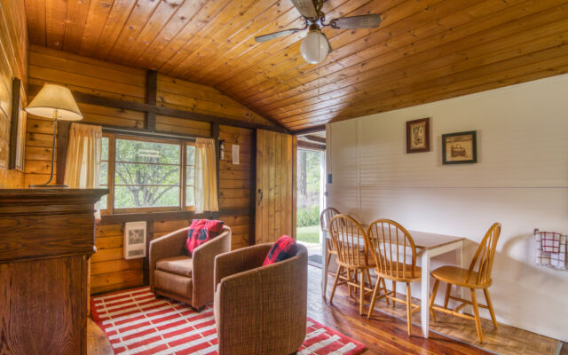 Small red cabin with two red outdoor lounge chairs outside. Trees and greenery surrounding.