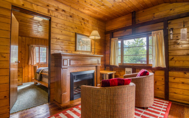 Small red cabin with two red outdoor lounge chairs outside. Trees and greenery surrounding.