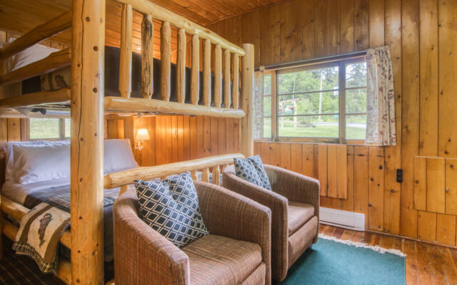 Small red cabin with two red outdoor lounge chairs outside. Trees and greenery surrounding.
