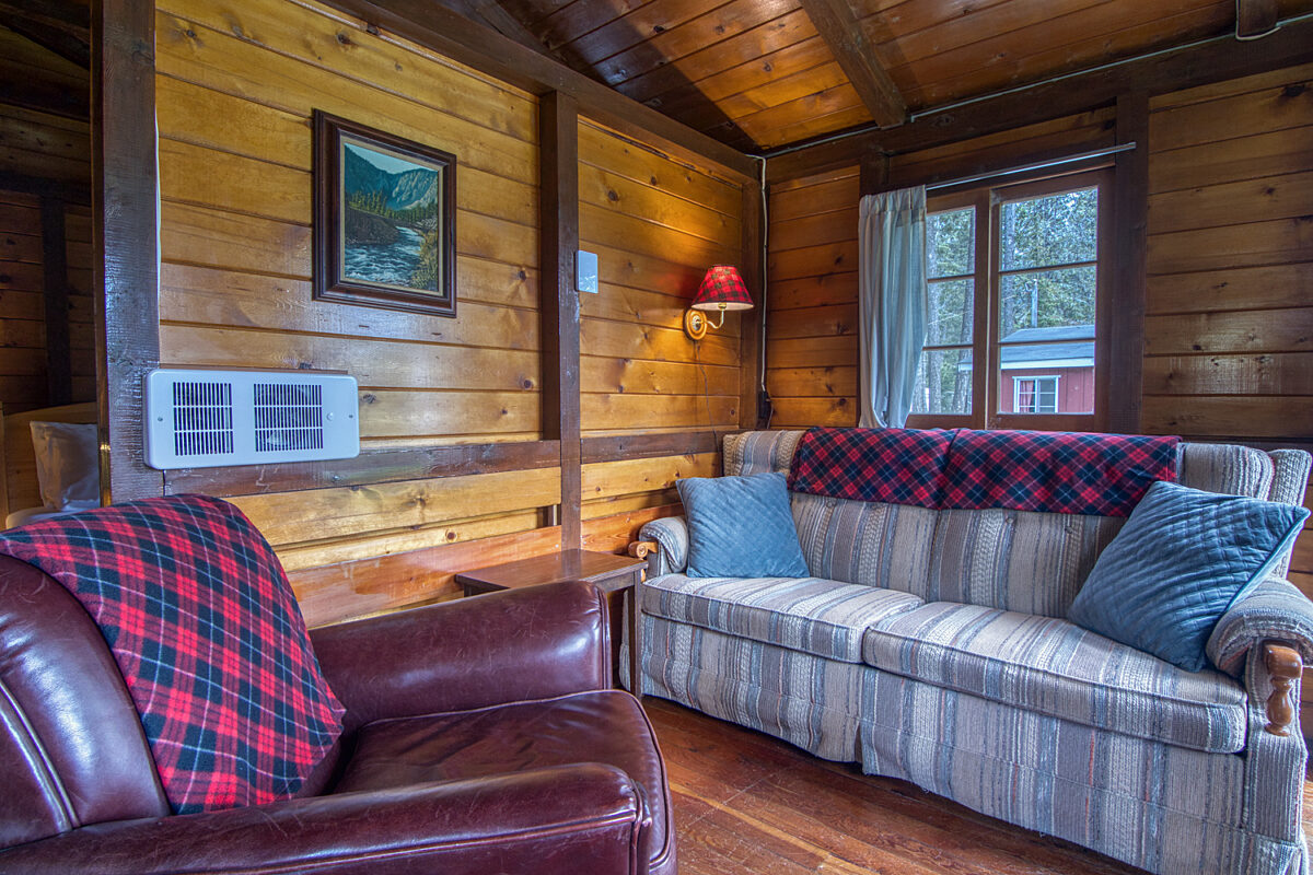 Wood panelled cabin living room couch and leather chair, window to the right.