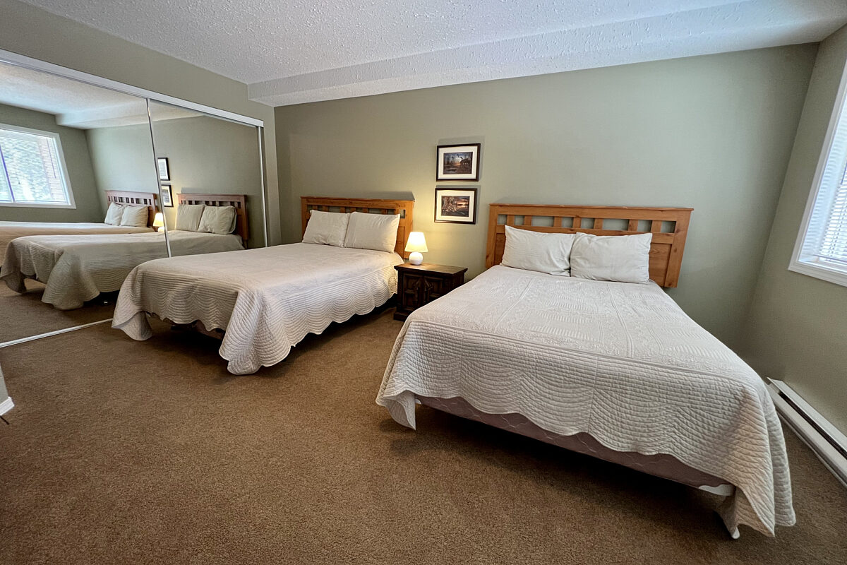Two double beds with white bedding in a capeted room with light sage walls.