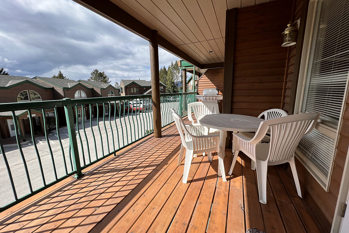 Patio with white outdoor furniture. Green railings overlooking parking area and other accommodation.