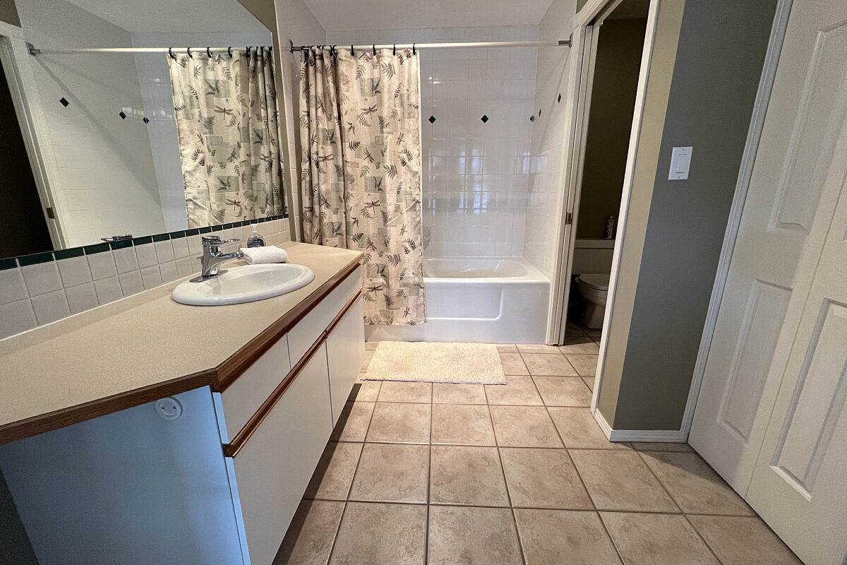 Bathroom with tile flooring, white vanity, mirror, and cupboards.