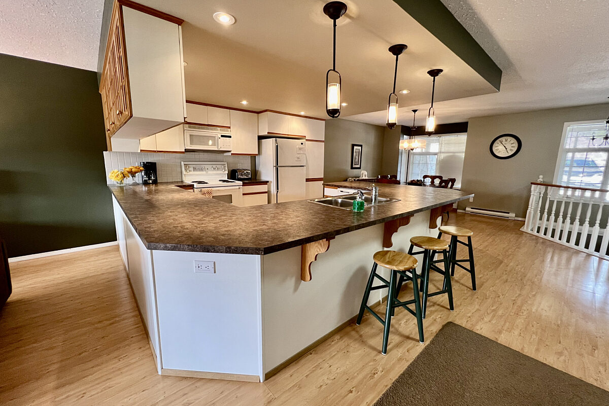 Kitchen featuring white island, barstools, and black countertops. Hanging lights above. Refrigerator and stove.