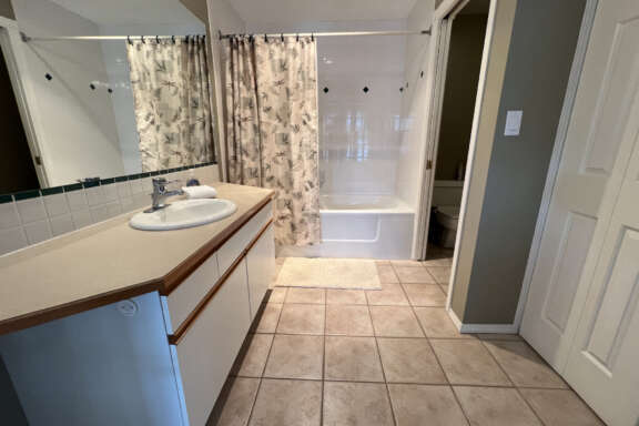 Bathroom with tile flooring, white vanity, mirror, and cupboards.