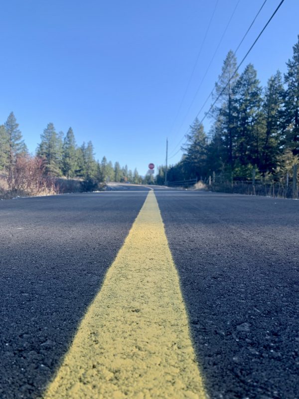 A long yellow line in the centre of a road. Blue sky.