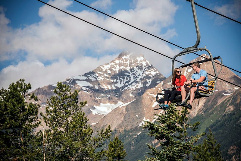two people riding a ski lift in the mountains in the summertime.