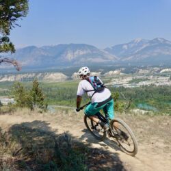 a man riding a bike down a dirt road. Blue sky.