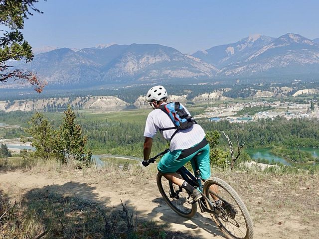 a man riding a bike down a dirt road. Blue sky.