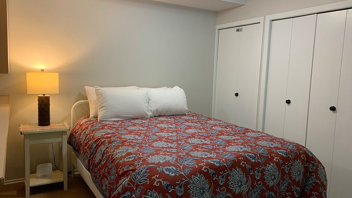 Queen bedroom with red bedding, bedside table, and lamp
