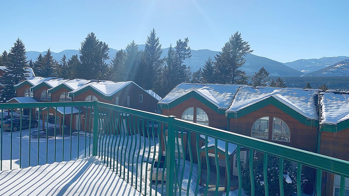 Deck in the winter time with snow and views of other accommodations, mountains, trees, and blue sky.