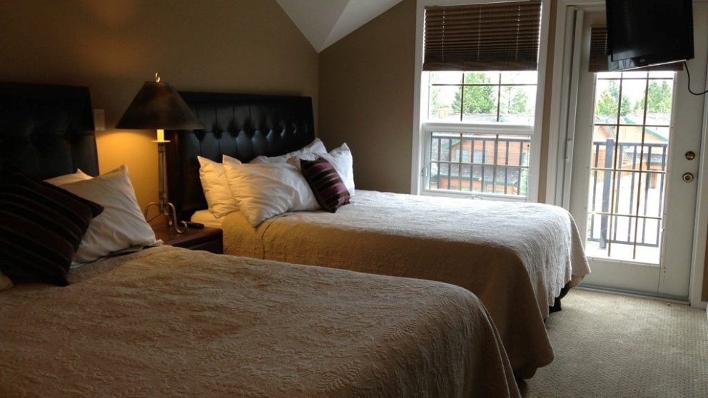 Bedroom with 2 queen beds, window to the rear of the room. Bedside table with lamp between beds.
