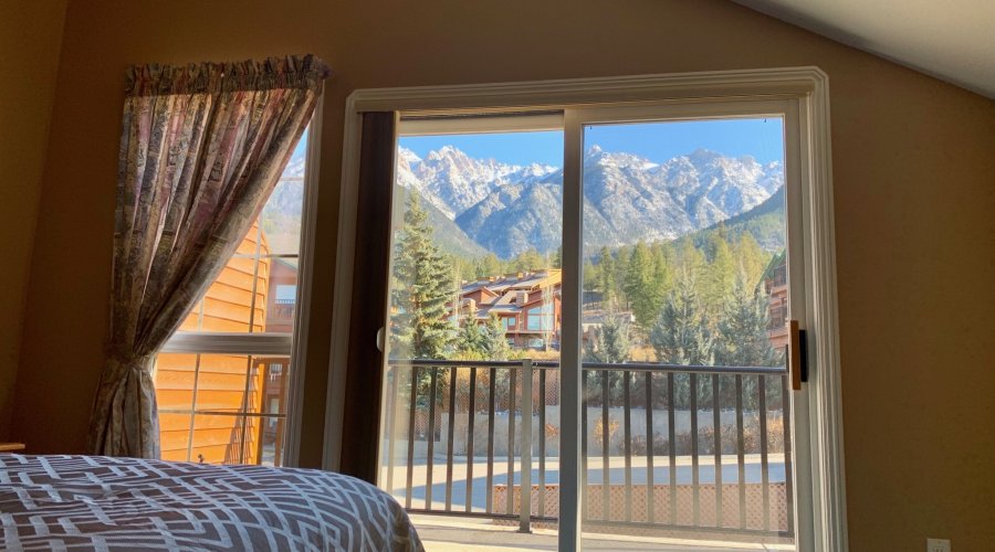 Bedroom with windows open to view a mountain range and trees in the distance.