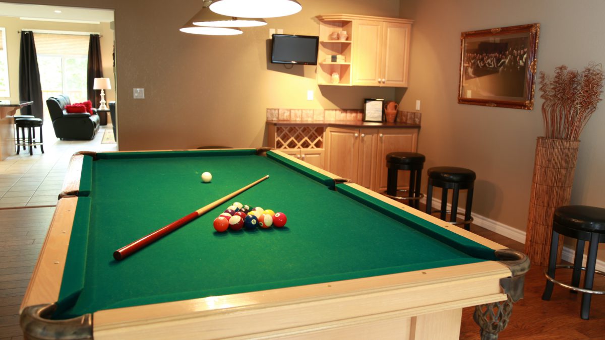 Pool table with stick and balls in recreation area of house.