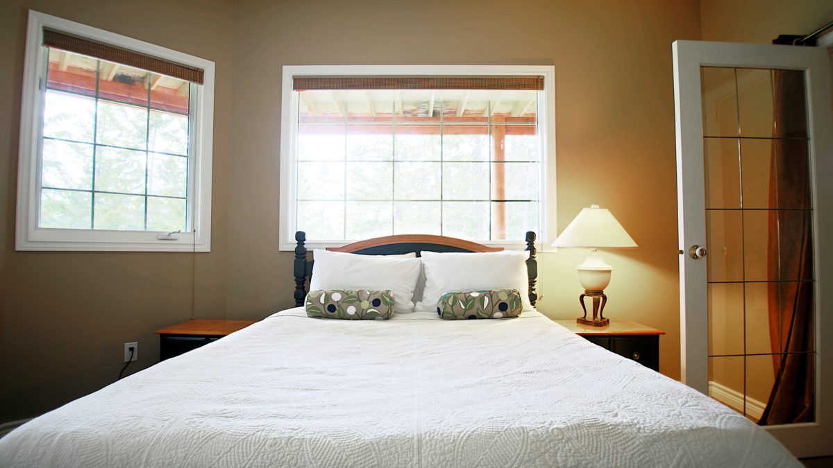 Bedroom with bed, white bedding, and two windows above.