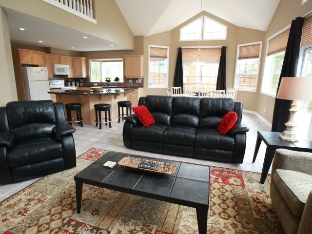 Living room with black leather couch, black leather chair, coffee table, and red pillows.