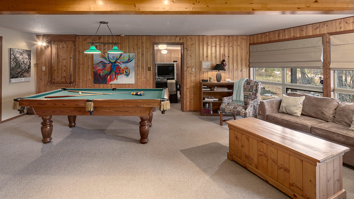 Recreation room with pool table, bar area, couch, windows to the right, and seating.