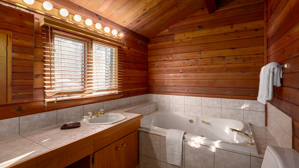 Rustic bathroom with bathtub and sink. Mirror with lights above sink. Wood panelling on the walls.