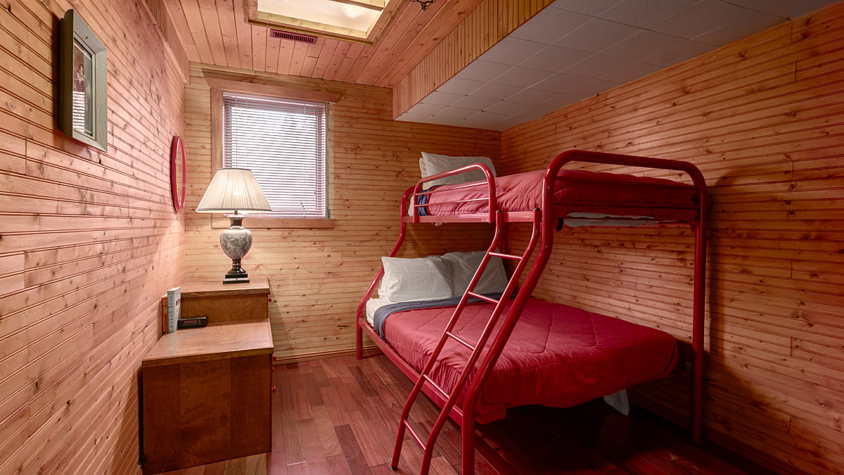Wood panelled bedroom. Bunk bed with queen on the bottom half and twin on the top. Red bedding.
