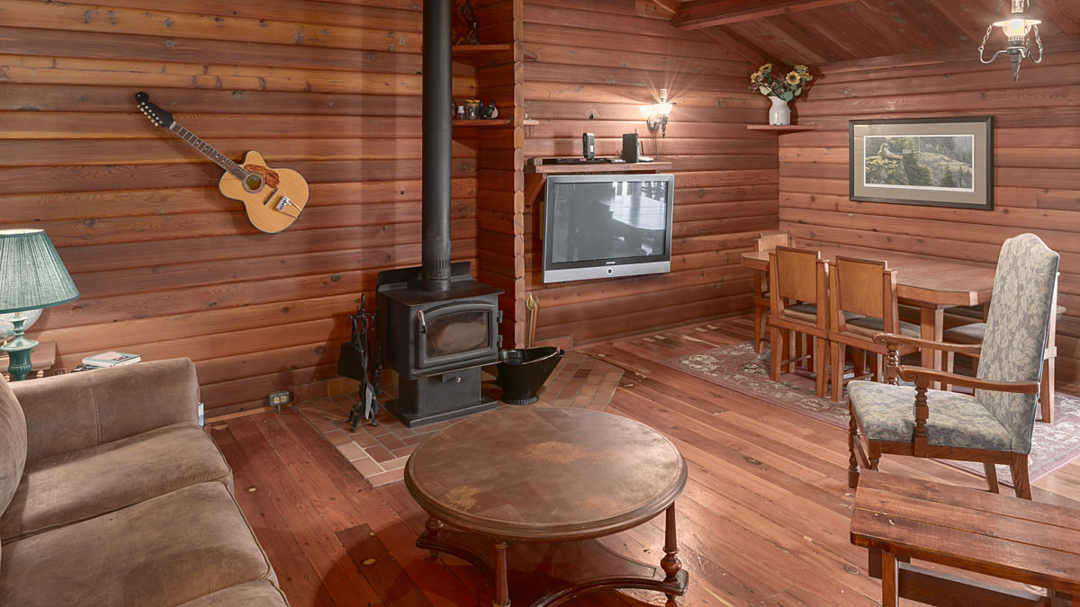 Rustic cabin living space with wood stove, tables, chairs, and assorted seating.