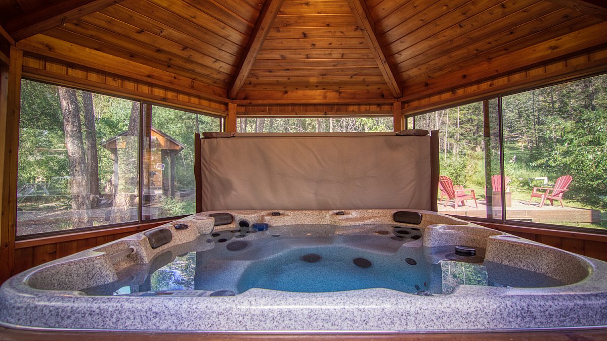 Hot tub under wood panelled gazebo. Lid removed to display jets and water.