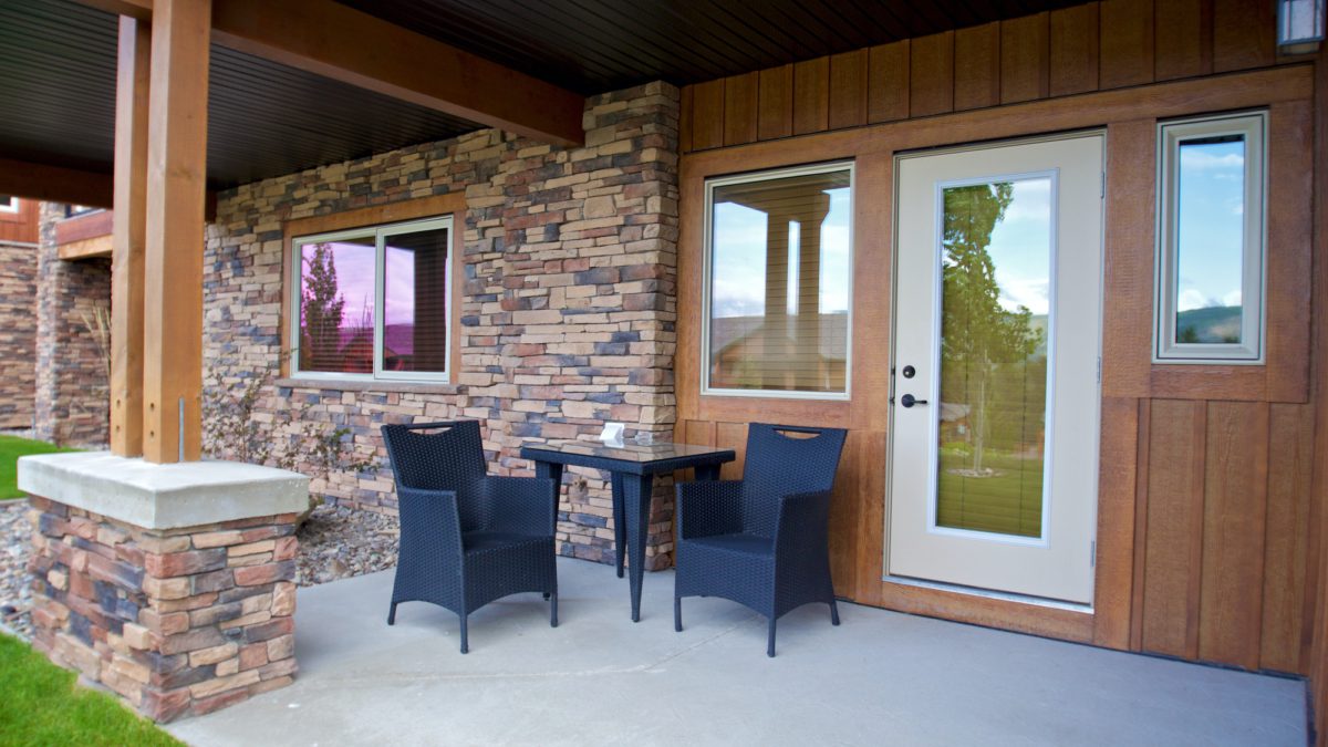 Patio with two black chairs and coffee table. White door leads to the interior. Brick exterior of house.