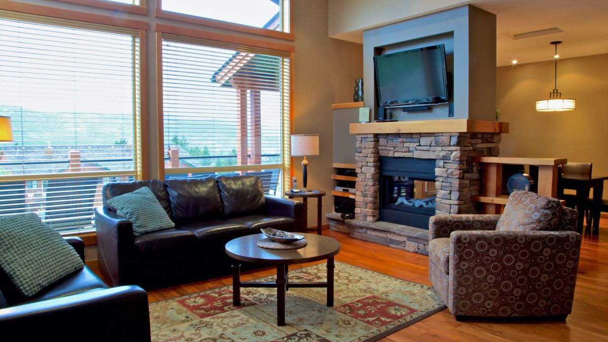 Living room area with couches, windows to the left, stone fireplace and television.